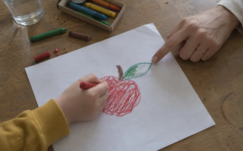 La mano di un bambino disegna una mela e la nutrizionista indica la foglia